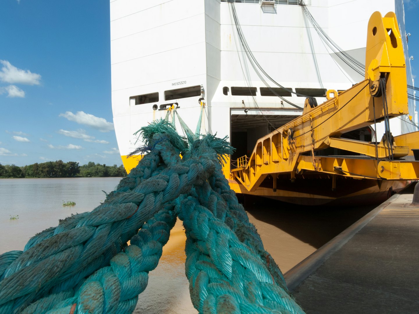 Thick turquoise ropes secure a cargo ship to a concrete dock.