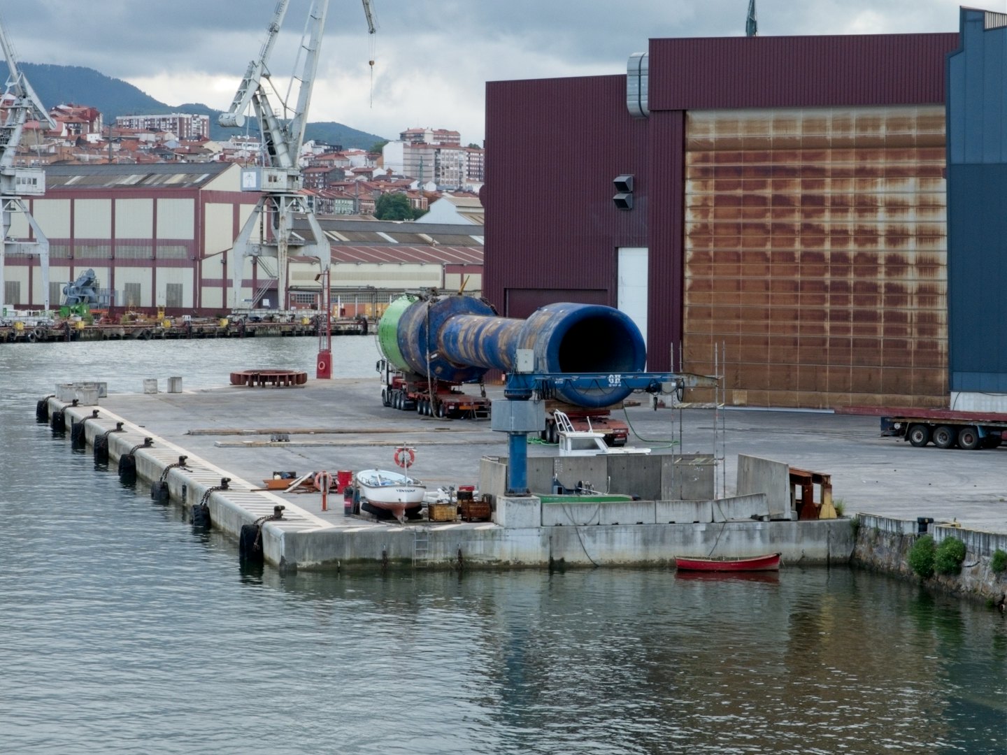 Industrial cargo sits on a truck at a busy harbor.
