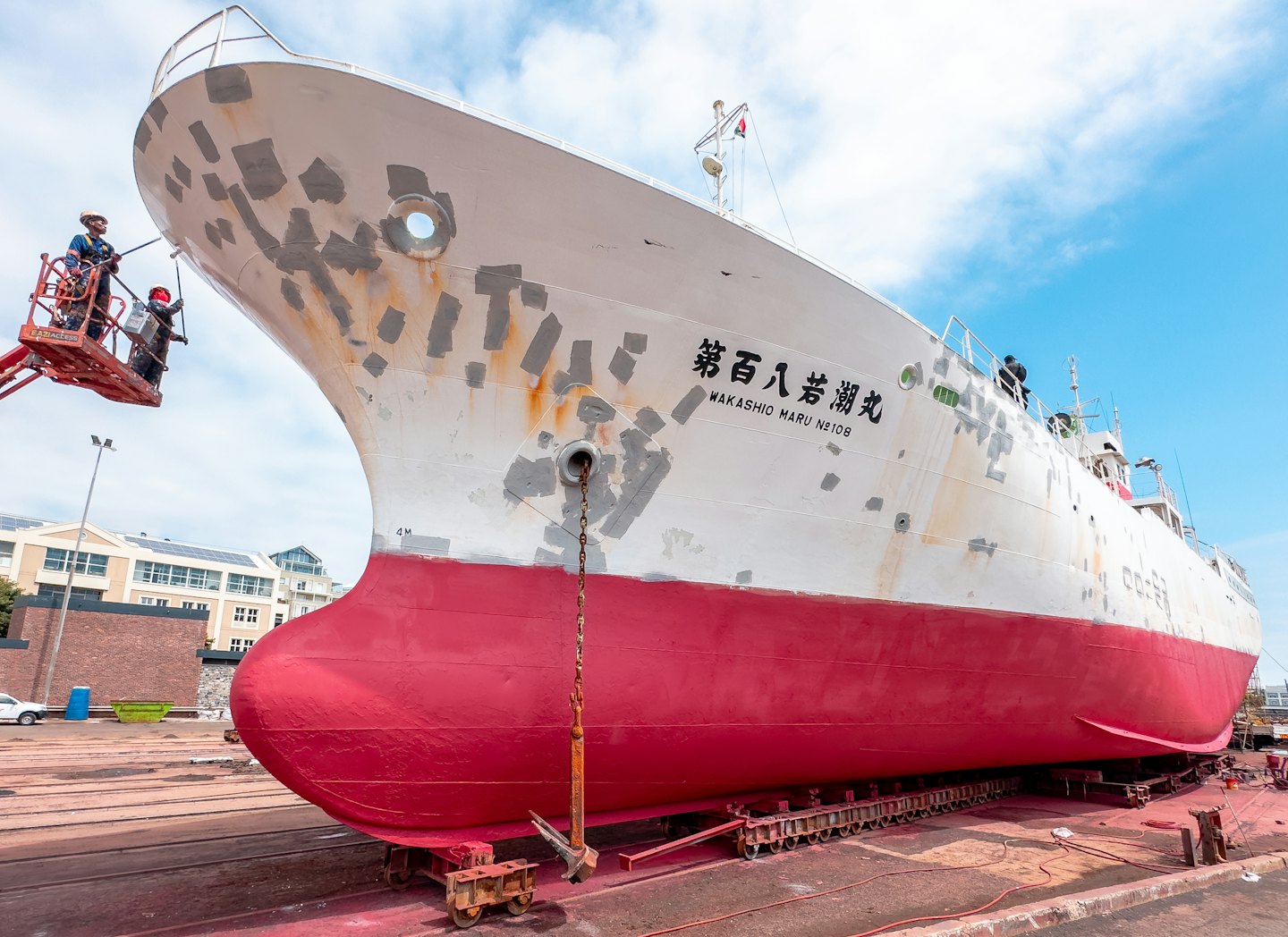 Workers in safety gear paint a large ship in dry dock.